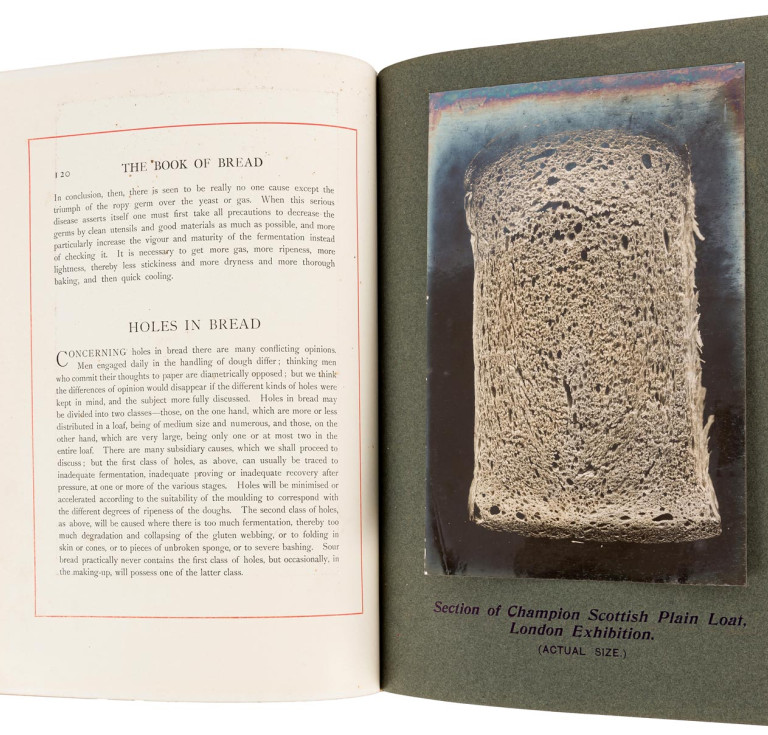 Silver bromide print of a loaf of bread on black card, facing a page of text, from Owen Simmons' "The Book of Bread".